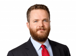 Man in a dark suit and red tie, with short hair and a beard.