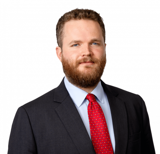 Man in a dark suit and red tie, with short hair and a beard.